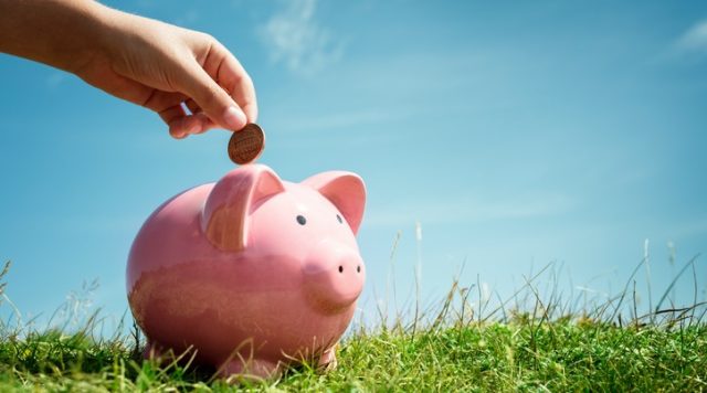 Child hand saving money in piggy bank
