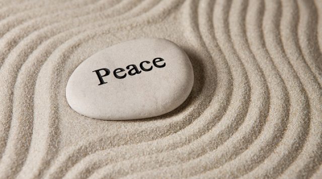 A stone with the word "peace" printed on it, in the middle of sand which is raked around the stone