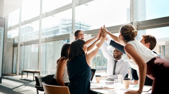 Shot of a group of businesspeople high fiving while sitting in a meeting